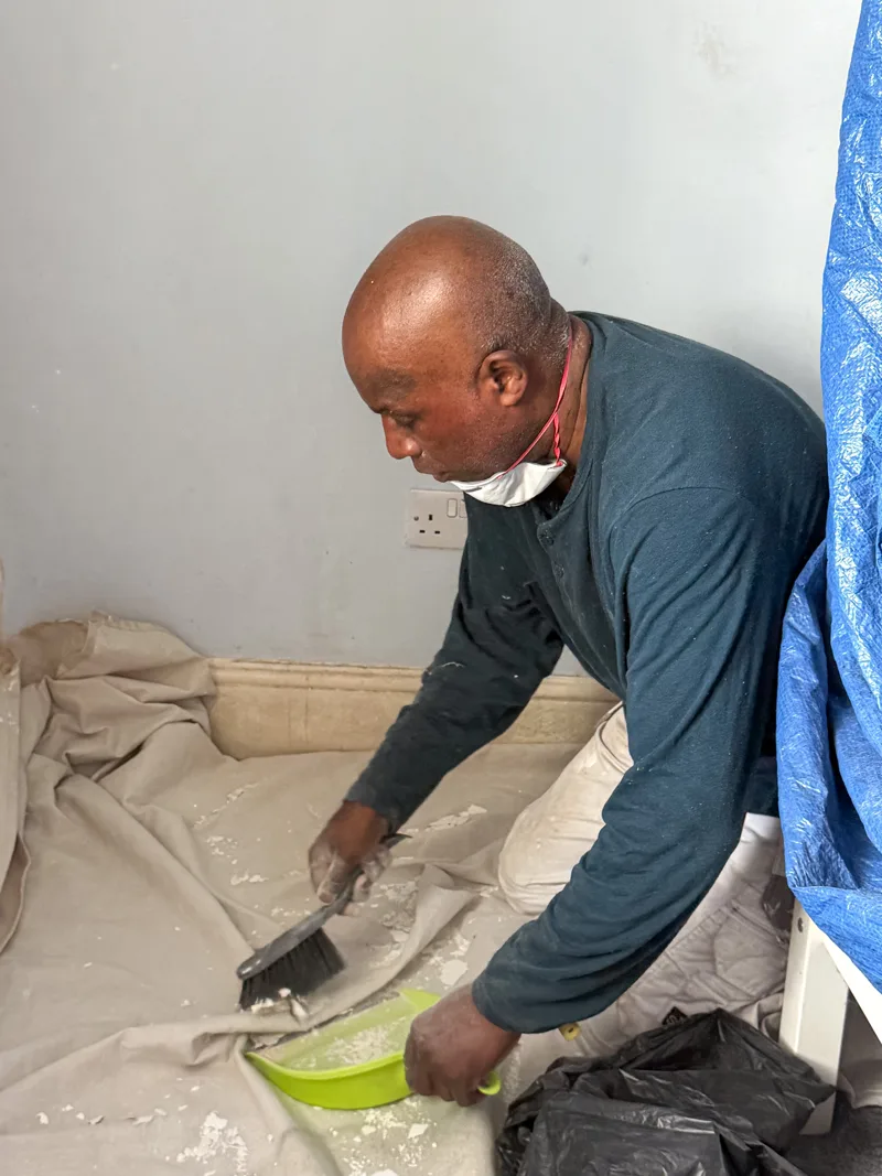 Roger brushing paint debris into a dustpan with protective sheets around the work area